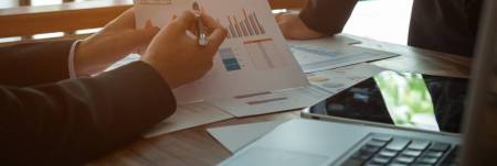 Two individuals, at a table, reading through graphs and charts displaying data.