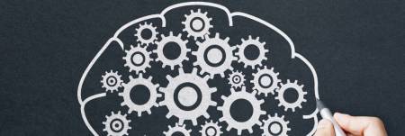 A hand drawing a brain with gears on a blackboard.