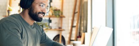 A person wearing headphones sits at a table and works remotely on their laptop.