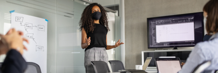 A woman leads a meeting in a conference room, standing in front of a screen.