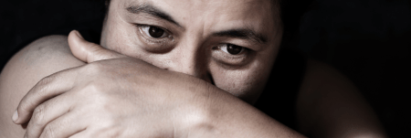 A person is seen in the dark, resting their head on their arm, with their hand wrapped around their arm.