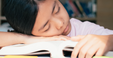 A young girl is asleep on her book.