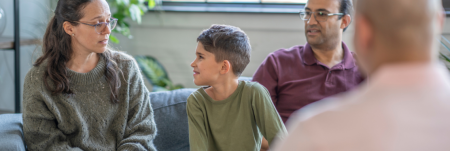 A mother and father sit together with their child across from a practitioner. The mother talks to her son.