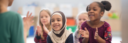 A group of children smile and follow their teacher's hand movement.