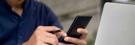 A person works on their laptop, holding a pen and their phone.