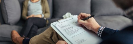 A practitioner sits across from their client. They take notes on their clipboard.