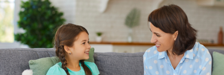 A young girl sitting on a couch next to a practitioner. They smile at each other.