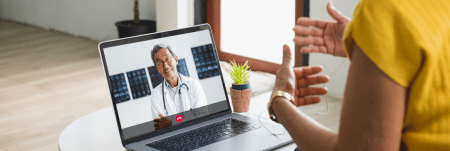 A doctor and their patient talk over a video call. The doctor is seen listening and smiling on screen.