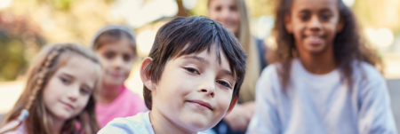 A child sitting outside with their friends. They all face forward and smile.