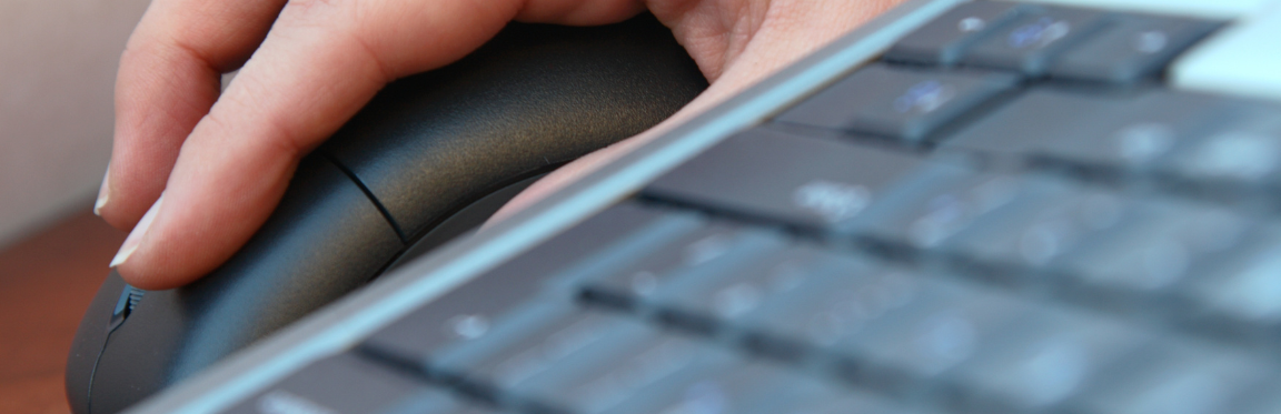 A person's hand resting on a mouse next to a keyboard.