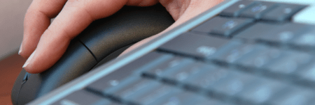 A person's hand resting on a mouse next to a keyboard.