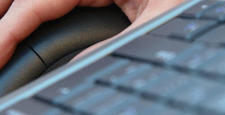 A person's hand resting on a mouse next to a keyboard.