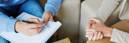 A psychologist is sitting down with their patient. The psychologist is filling out a form.