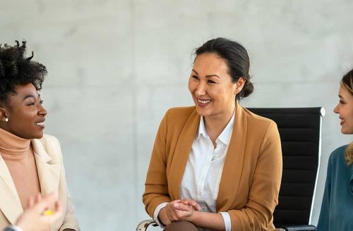 Group of professionals in a casual business meeting, smiling and engaged in discussion in a modern office.