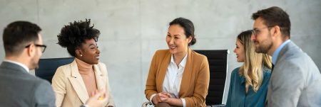 Group of professionals in a casual business meeting, smiling and engaged in discussion in a modern office.