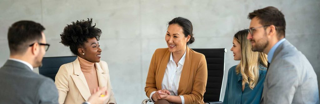 Group of professionals in a casual business meeting, smiling and engaged in discussion in a modern office.