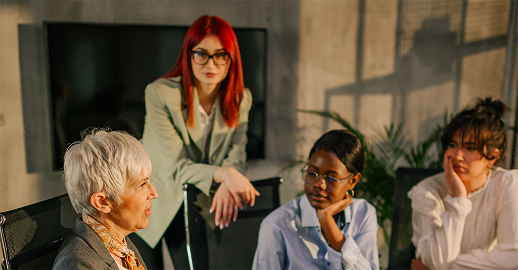 Four individuals engaged in a discussion, with one person speaking while others listen attentively in a modern office or meeting room.
