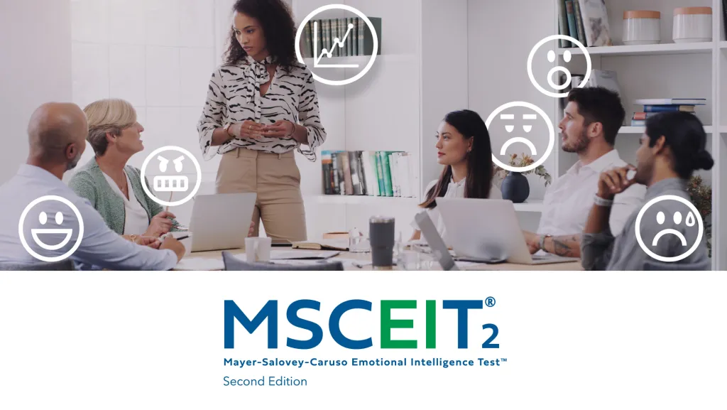 People sit around a conference table listening to a presenter at the front of the room. Emotion‑themed icons—such as happy, sad, surprised, and confused faces—are overlaid around the group. The MSCEIT² Mayer‑Salovey‑Caruso Emotional Intelligence Test logo appears below the scene.
