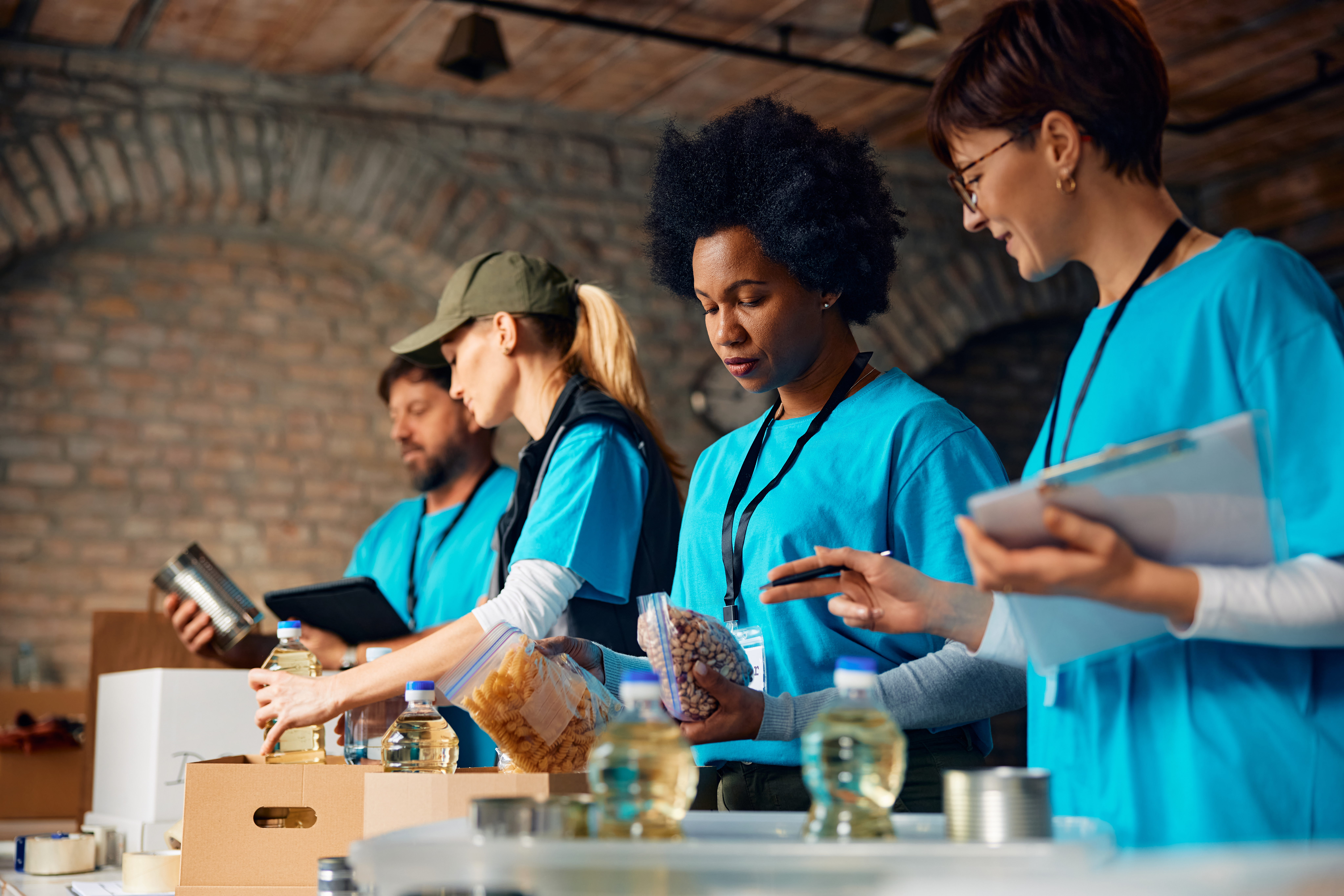 Group of charity workers sorting food into boxes while volunteering at community center. Focus is on African American woman.